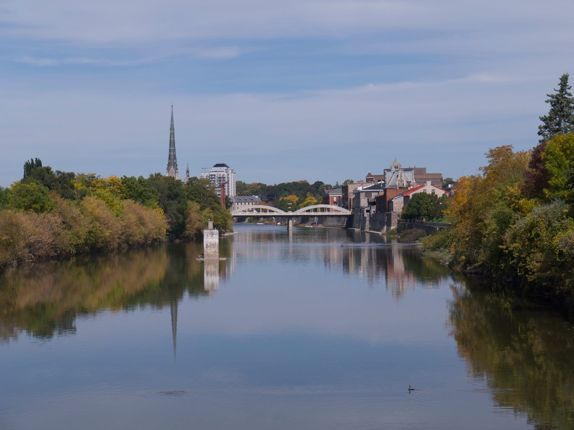 The Grand River and downtown Galt in Cambridge seen from the Cedar Street bridge, with a church spire and the Main Street Bridge in the distance